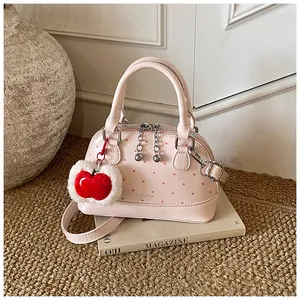 Pink polka dot mini handbag with red apple plush charm on a styled white background