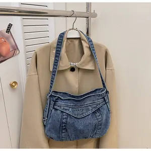 Détail du sac hobo en jean bleu avec broderie du logo sur un fond de manteau kaki