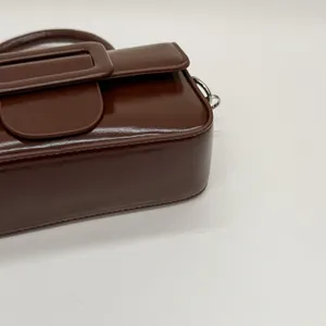 Detail view of high-gloss dark brown leather bag with signature oversized square buckle