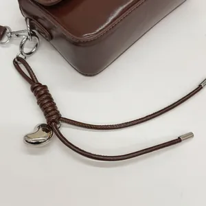 Detail of dark brown glossy leather handbag with silver heart pendant and metal buckle