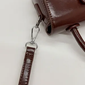 Detail of silver metal lobster clasp and reinforced stitching on dark brown leather bag