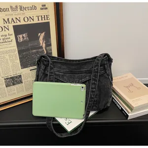 Comparaison de taille d'un sac bandoulière en denim noir avec une tablette tactile