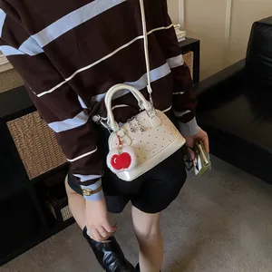Polished white shell bag with red dots and cherry charm accessory in a lifestyle view