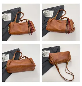 Detail view of a vintage brown leather Boston bag with metal eyelets and a woven charm