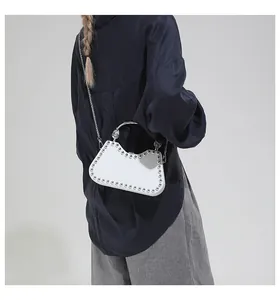 Detail of white studded shoulder bag featuring silver metal ring handle and chain strap