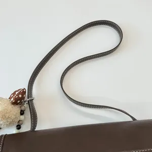 Dettaglio della borsa a tracolla marrone scuro con cuciture bianche e ciondolo peluche