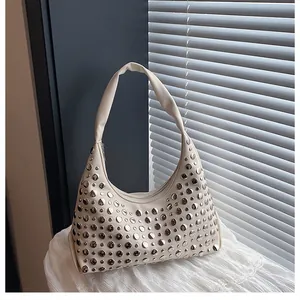 Dettaglio ravvicinato di borchie metalliche argentate su borsa hobo color bianco crema