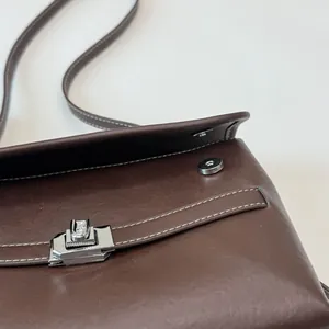 Dettaglio della borsa tote in pelle marrone con chiusura a rotazione e cuciture bianche