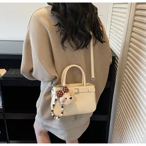 Detail showing beige leather handbag with teddy bear charm on knit sweater outfit