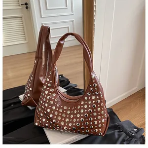 Dettaglio borsa hobo marrone con borchie argentate e cerniera appoggiata su libri bianchi