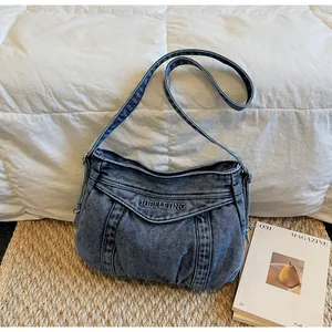 Gros plan du sac bandoulière en denim délavé avec broderie de marque et design plissé
