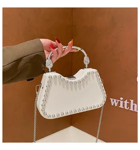Close-up of white leather handbag featuring silver rivets and ornate metal handle