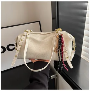 Close-up of white lychee texture leather Boston bag with woven tassel and key charm