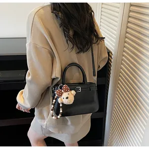 Black bucket bag with metal buckle and cute bear charm shown in a real-life setting