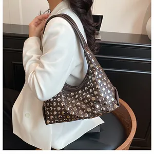Dettaglio di una borsa tote marrone scuro con borchie indossata da una modella in blazer