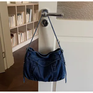 Détail du sac hobo en denim bleu avec broderie suspendu à une poignée de porte