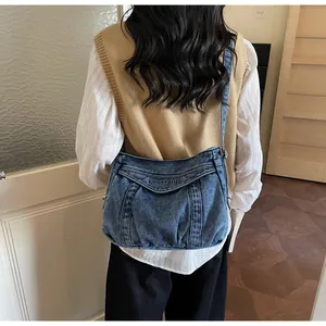Gros plan du sac bandoulière en jean délavé bleu avec broderie et base plissée robuste