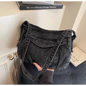 Détail du sac à bandoulière en denim noir délavé avec broderie de lettres blanches