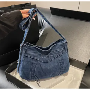 Détail du sac à épaule en jean bleu avec plis verticaux et broderie sur le rabat avant