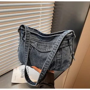 Détail du sac en jean bleu vintage avec logo brodé et large bandoulière confortable