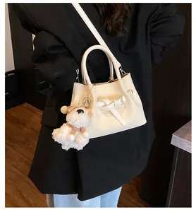 Détail du sac beige en cuir texturé avec breloque chien en peluche sur un manteau noir