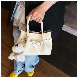 Détail du sac seau crème avec texture tressée, boucle et breloque en forme d'ours en peluche