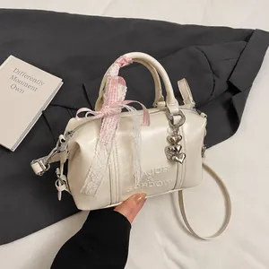 Detail showing cream Boston bag with logo, lace bow ribbon and heart charms