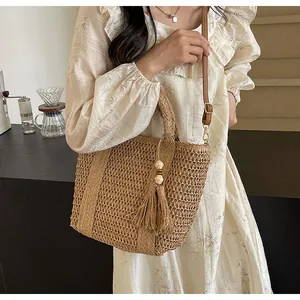 Detail of woven straw tote featuring tassel ornaments and wood beads on a textured surface