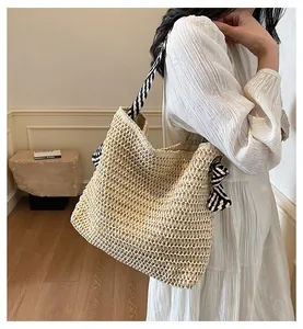 Detalle de un bolso tote grande de paja con correa de rayas y lazo decorativo de moda