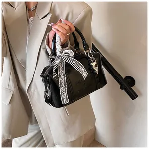 Close-up of black patent leather Boston bag with a ribbon bow and metal heart charm