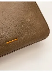 Detailed close-up of brown textured leather and golden metal logo plate on tote bag