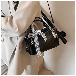 Detail of black glossy pillow bag with striped lace bow and silver heart charm