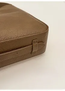 Detail of brown textured leather tote bag showing base stitching and side strap