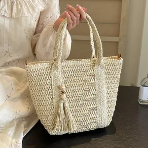 Beige woven straw tote bag with elegant tassel detail and top handles for summer vacation