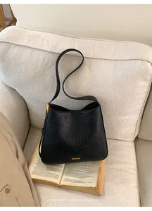 Close-up of black textured leather bucket bag with golden logo on white fabric background