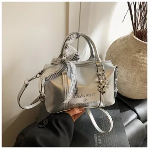 Close-up of silver cylinder bag with embossed logo, lace bow, and heart charms
