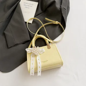 Detail van lichtgele vierkante crossbodytas met kanten strik en parel hartvormige hanger