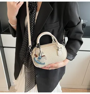 Detail of a creamy white leather bowling bag with a rocking horse charm and slim strap