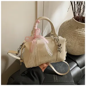 Detail of cream leather Boston bag featuring a lace bow, heart charm, and embossed logo