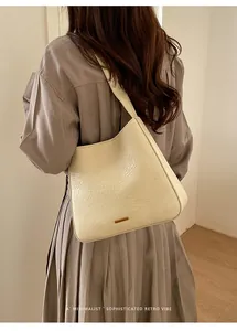 Close-up of cream textured leather shoulder bag featuring a rectangular gold metal logo plaque