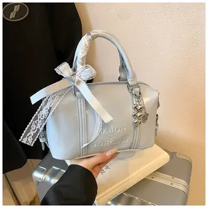 Detailed view of blue boston bag with embossed logo, lace bow, and heart metal charm