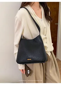 Detail of black pleated leather tote bag with gold logo plate on a fashion model