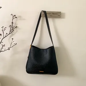Close-up of black textured tote bag with gold hardware detail on minimalist wall