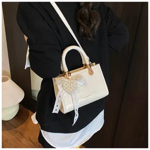 Detail van de crème crossbodytas met parelhartje en kanten strik op het gevlochten handvat