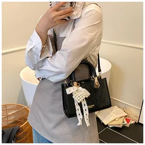 Detail van een chique zwarte leren crossbodytas met kanten strik en parel hart hanger