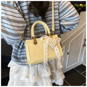 Detail van een crème PU-tas met geweven handvat en een kanten strik met parelhanger