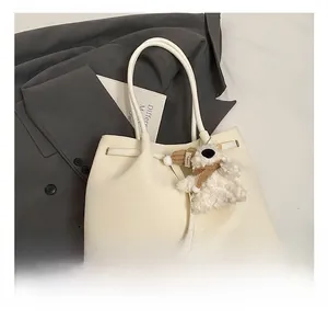 Close-up of white woven leather tote bag with plush puppy charm on grey suit background
