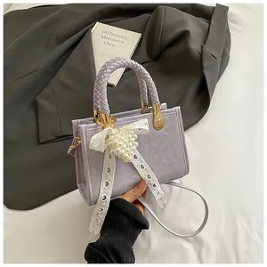 Detail van lichtpaarse tas met gevlochten handvat en parel-kant strik hanger sieraad