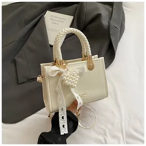 Detail van crème crossbodytas met geweven handvat en parelmoeren hartjeshanger