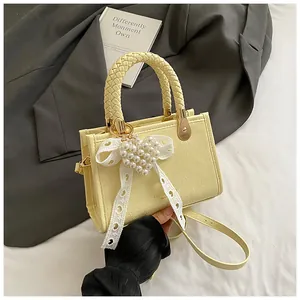 Detail van lichtgele crossbodytas met geweven handvat, parelhart hanger en kanten lint
